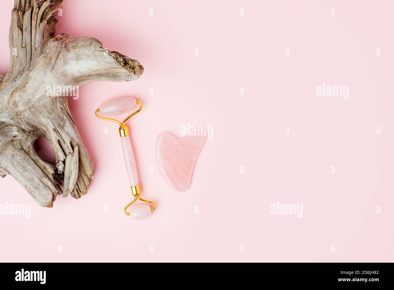 Masseur à quartz rose Gua Sha et rouleau de jade sur fond rose pastel. Pierre de Jade pour le soin du visage et du corps. Pousse horizontale, racine de plante ligneuse, élégant Banque D'Images