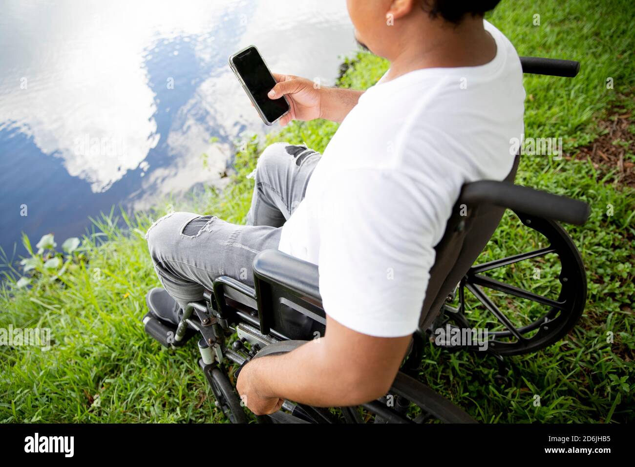 jeune homme en fauteuil roulant avec téléphone portable à la main face à un lac Banque D'Images