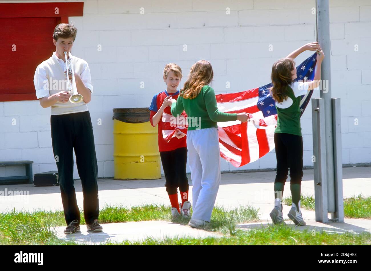 Un groupe d'enfants se réunit pour élever les américains drapeau des états-unis sur un poteau de drapeau Banque D'Images