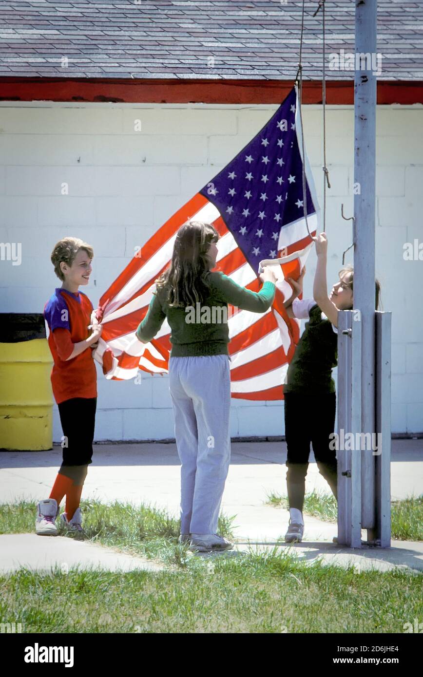 Un groupe d'enfants se réunit pour élever les américains drapeau des états-unis sur un poteau de drapeau Banque D'Images