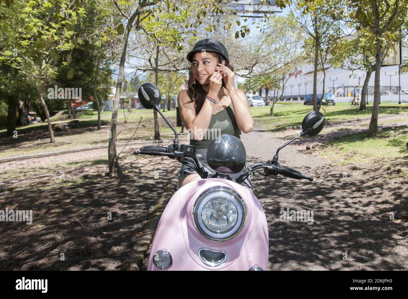 Jeune femme hispanique assise sur une moto électrique et de mise sur un casque Banque D'Images