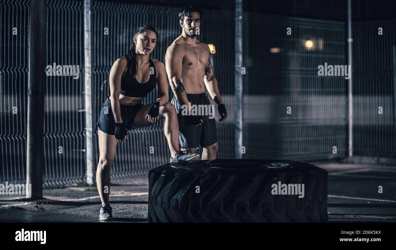 Belle forme physique énergique fille et musculaire Homme posant après des exercices dans un terrain de basket-ball extérieur clôturé. Ils rendaient un gros pneu lourd Banque D'Images