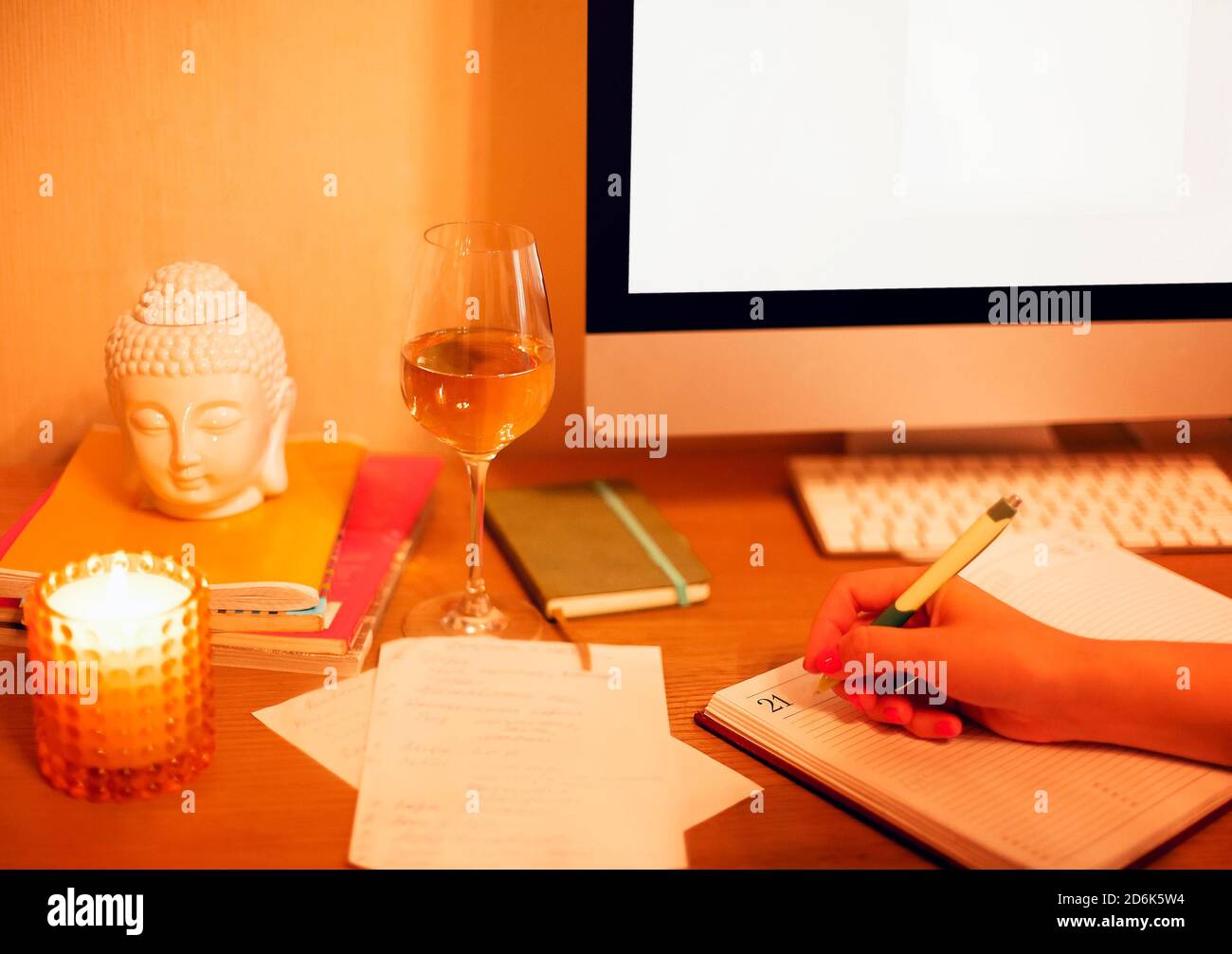 Femme méconnue assise à la table à la maison et écrivant organiser tout en planifiant la routine quotidienne et se détendre avec un verre de vin Banque D'Images