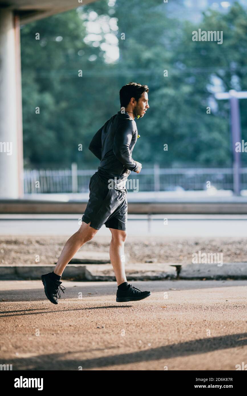 Le jeune sportif en tenue de sport est le jogging dans la rue. Il court dans un environnement urbain sous un pont avec des voitures en arrière-plan. Banque D'Images