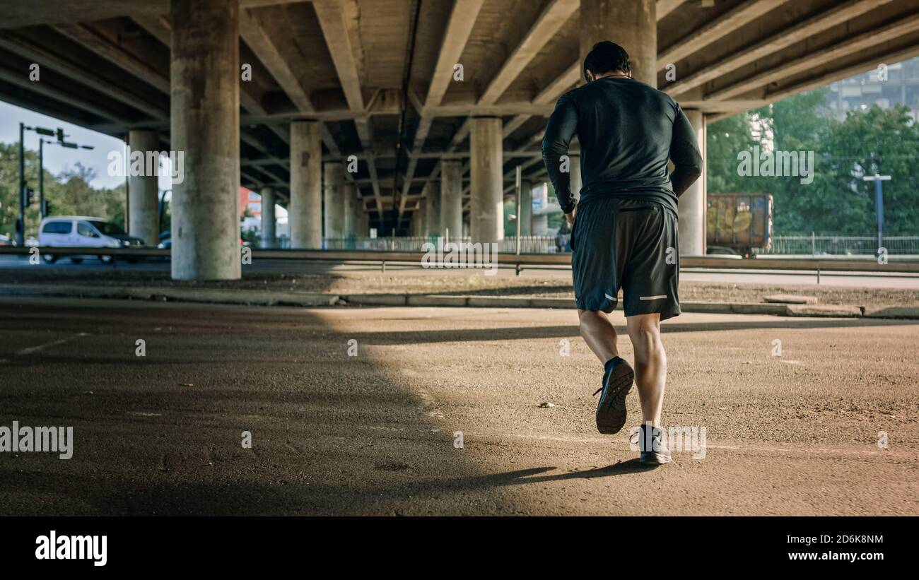 Photo d'un jeune homme athlétique dans un ensemble de jogging sportif dans la rue. Il court dans un environnement urbain sous un pont avec Cars dans le Banque D'Images