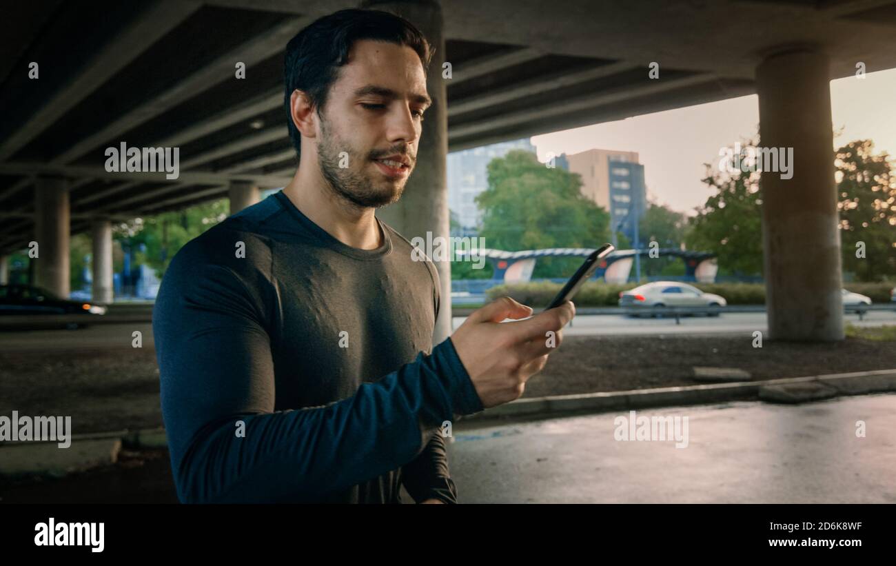 Athlétique muscle jeune homme dans le sport tenue de jogging dans une rue. Il utilise son smartphone. L'athlète court dans un environnement urbain sous un pont Banque D'Images