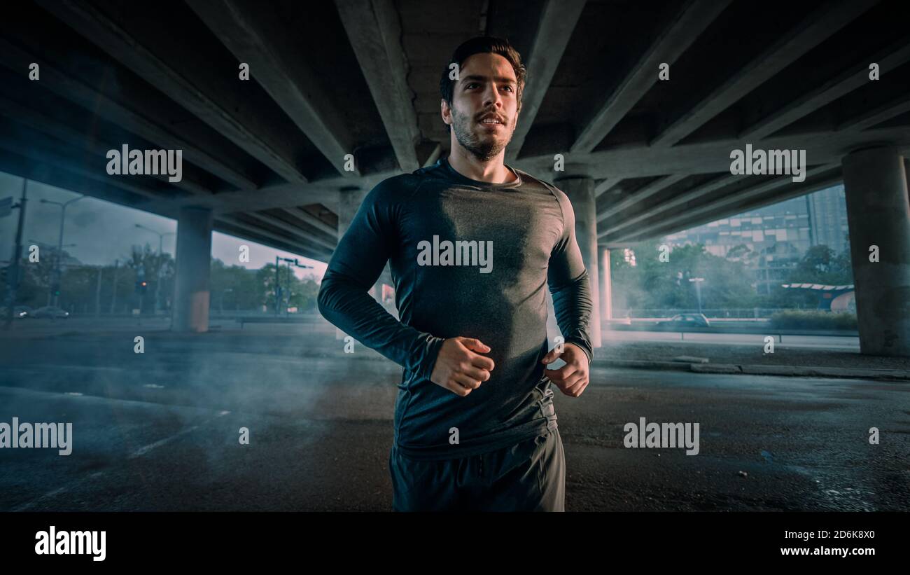Portrait prise d'un jeune homme athlétique musclé dans un ensemble de sport jogging dans la rue. Il court dans un environnement urbain sous un pont. Banque D'Images