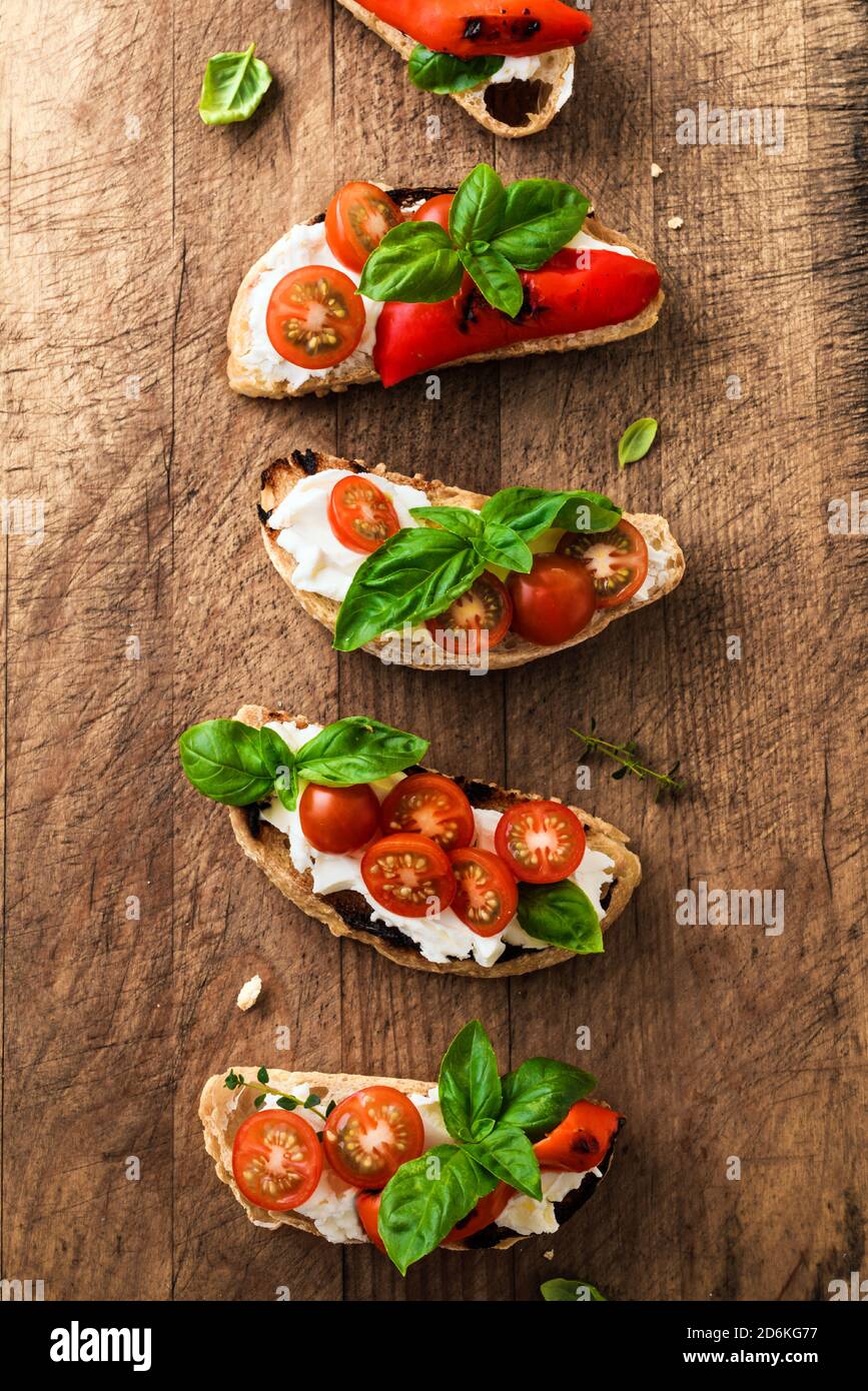 Sandwichs à la bruschetta avec tomates, fromage à la crème, paprika grillé et basilic sur fond de bois, vue du dessus. En-cas italien traditionnel - brusc grillé Banque D'Images