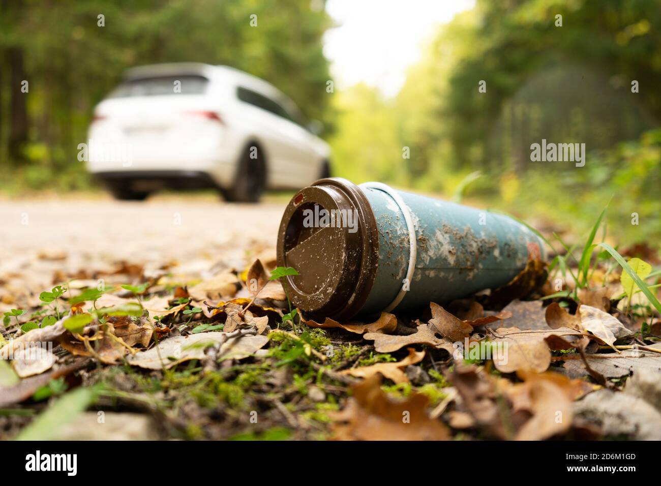 Vieille tasse de café jetable dans la forêt à côté de la route avec la voiture dans un fond. Recyclage du plastique, pollution et réchauffement climatique. Banque D'Images