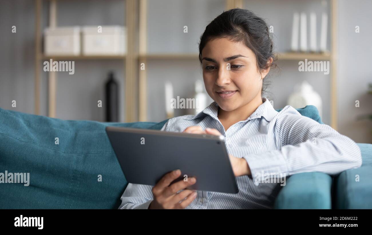 Femme indienne reposant sur un canapé tenant une tablette, faites vos achats en ligne Banque D'Images