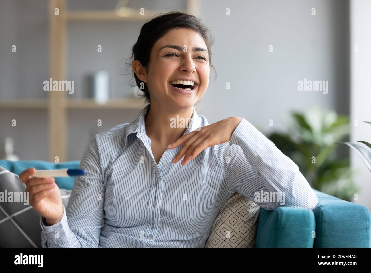 Femme indienne assis à l'intérieur tenir le test de grossesse rire se sent heureux Banque D'Images