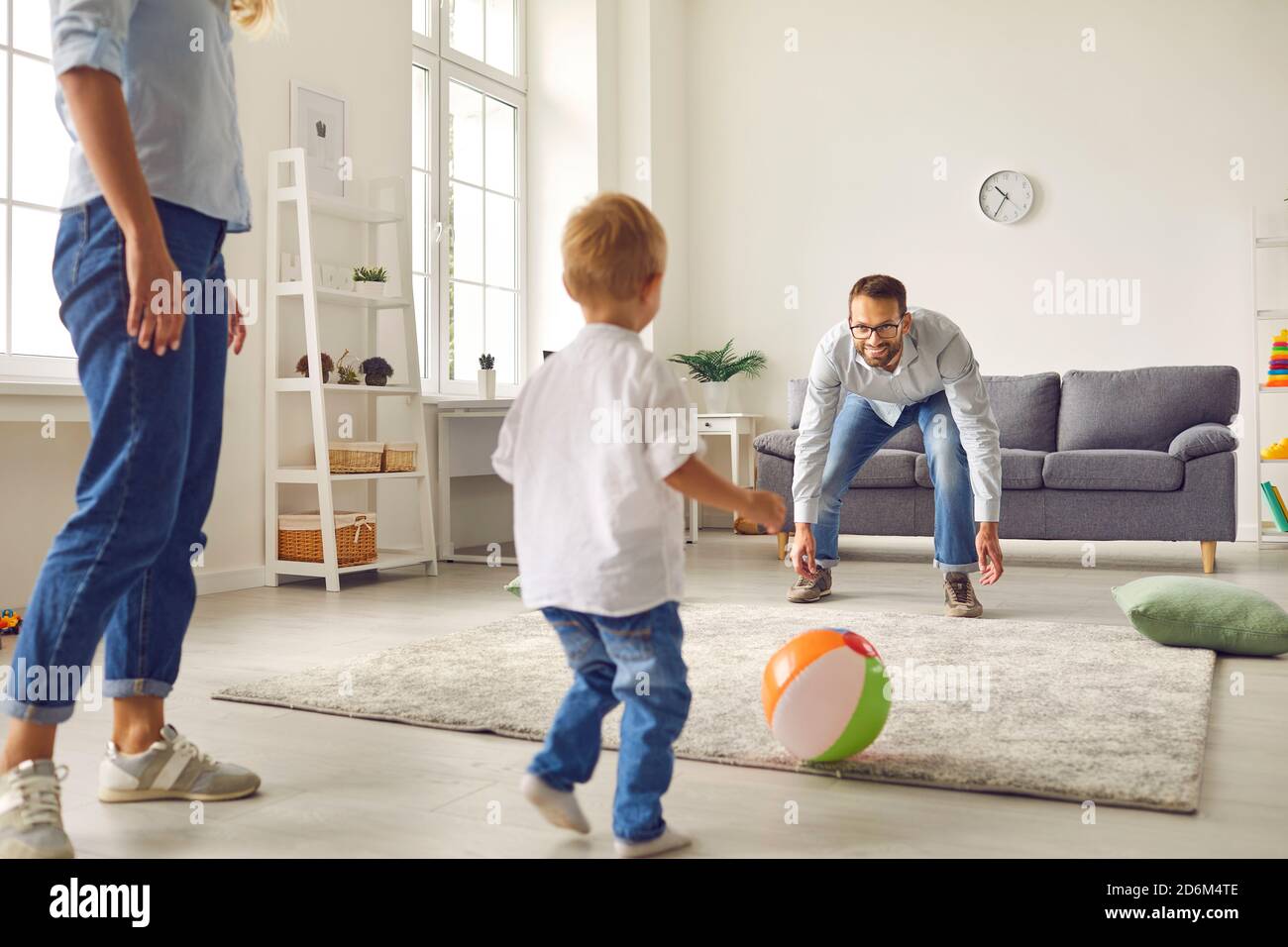 Joyeux jeune papa, maman et petit fils jouant au football avec ballon gonflable dans le salon Banque D'Images