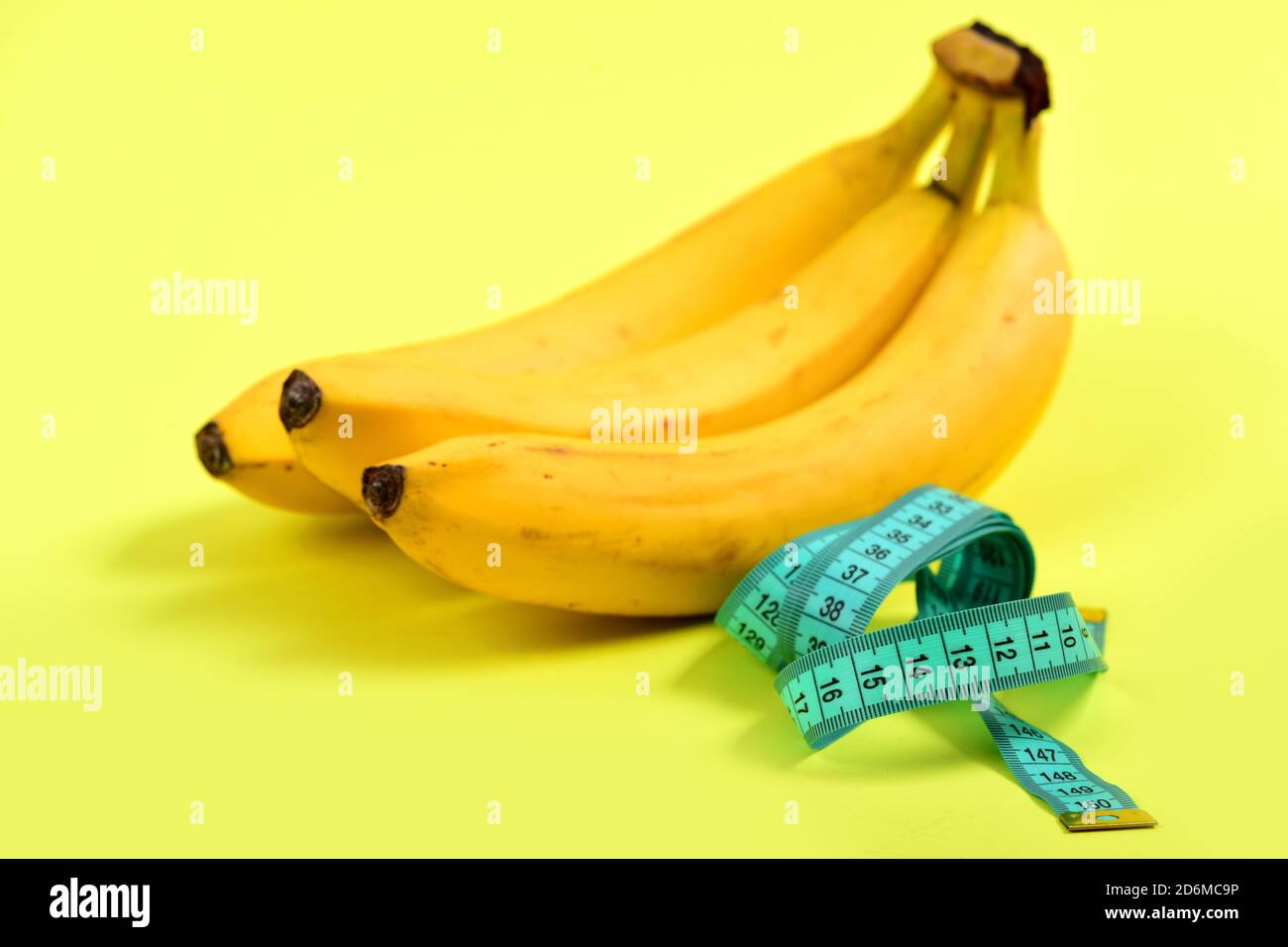 Pour la mesure de bande de couleur turquoise à côté de tas de bananes, isolé sur fond jaune clair. Concept de régime alimentaire faible en calories et vitamines alimentation Banque D'Images