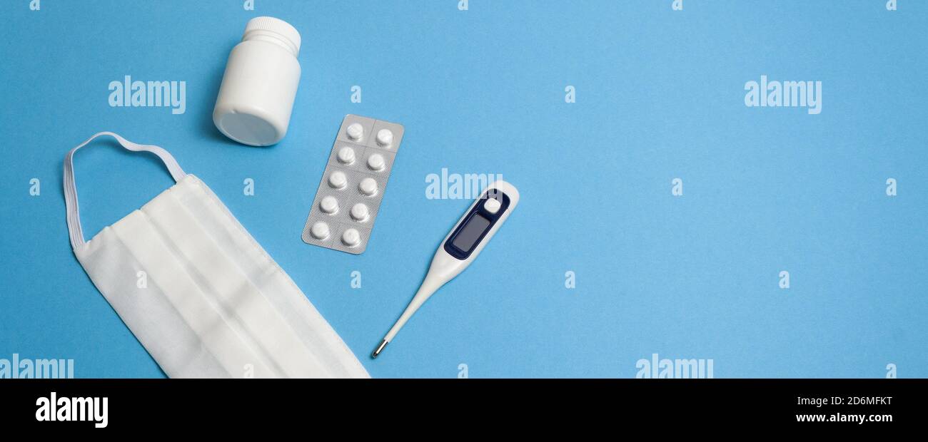 Équipement de protection contre la pandémie, coronavirus, vue de dessus. Masque médical, plateau de comprimés, pilules, flacon de capsule, thermomètre sur fond bleu i Banque D'Images