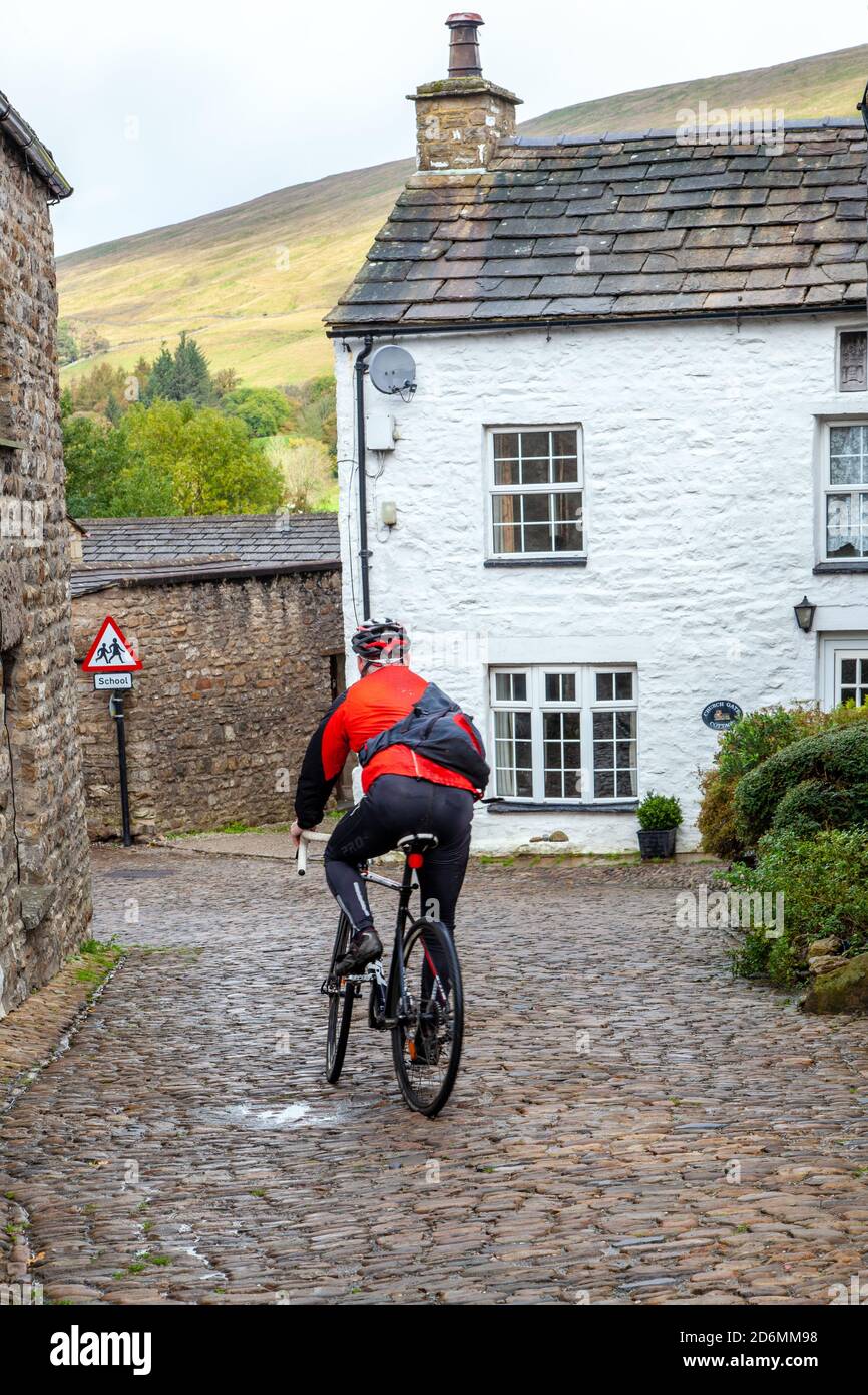 Personne à vélo à travers les rues pavées de la Cumbrian village de Dent à Dentdale dans le Yorkshire Dales Parc national Cumbria Banque D'Images