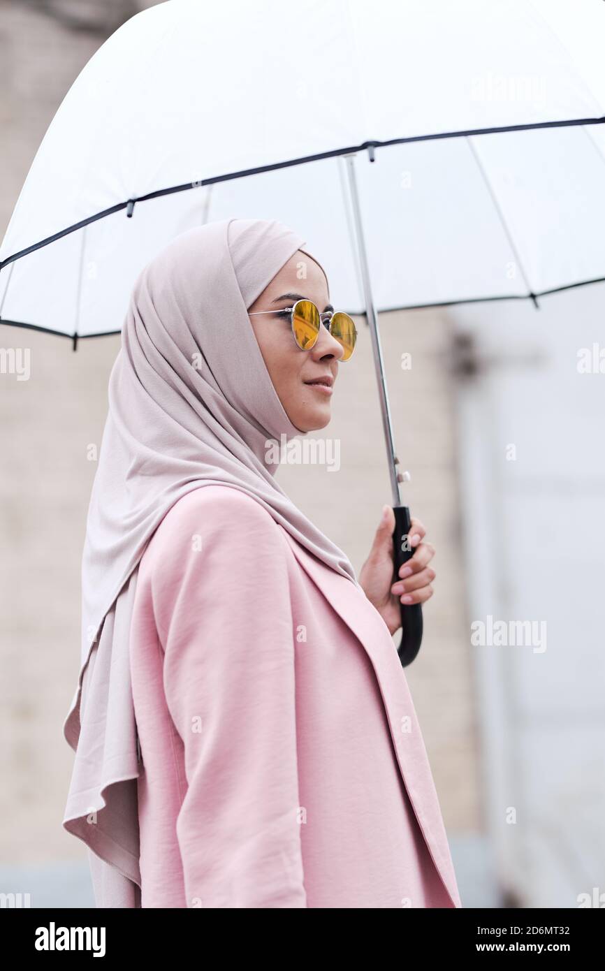 Jeune femme musulmane élégante en hijab, lunettes de soleil et gilet tenant un parapluie Banque D'Images