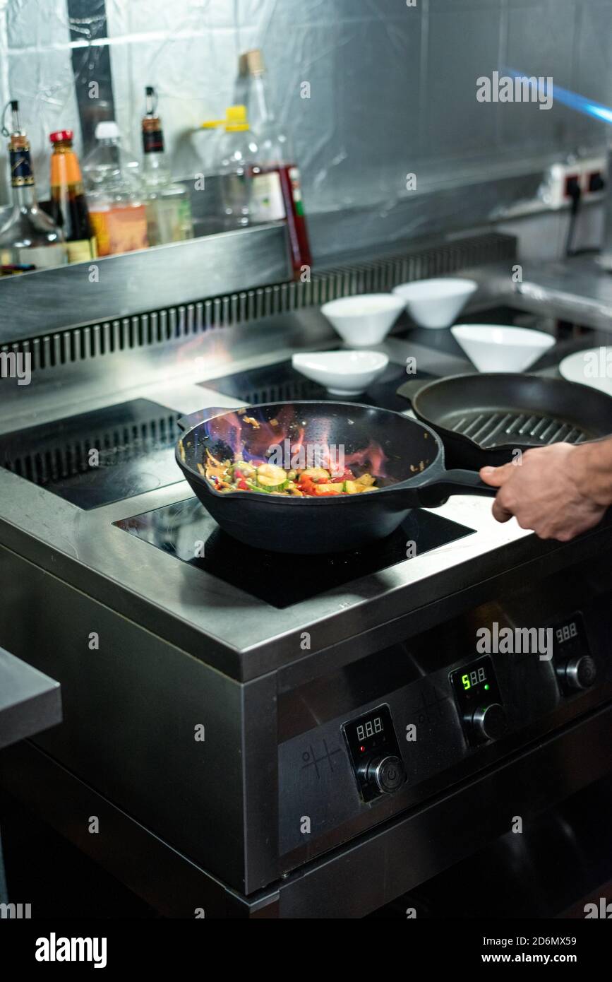 Main du jeune chef qui verse la poêle avec hachée légumes Banque D'Images