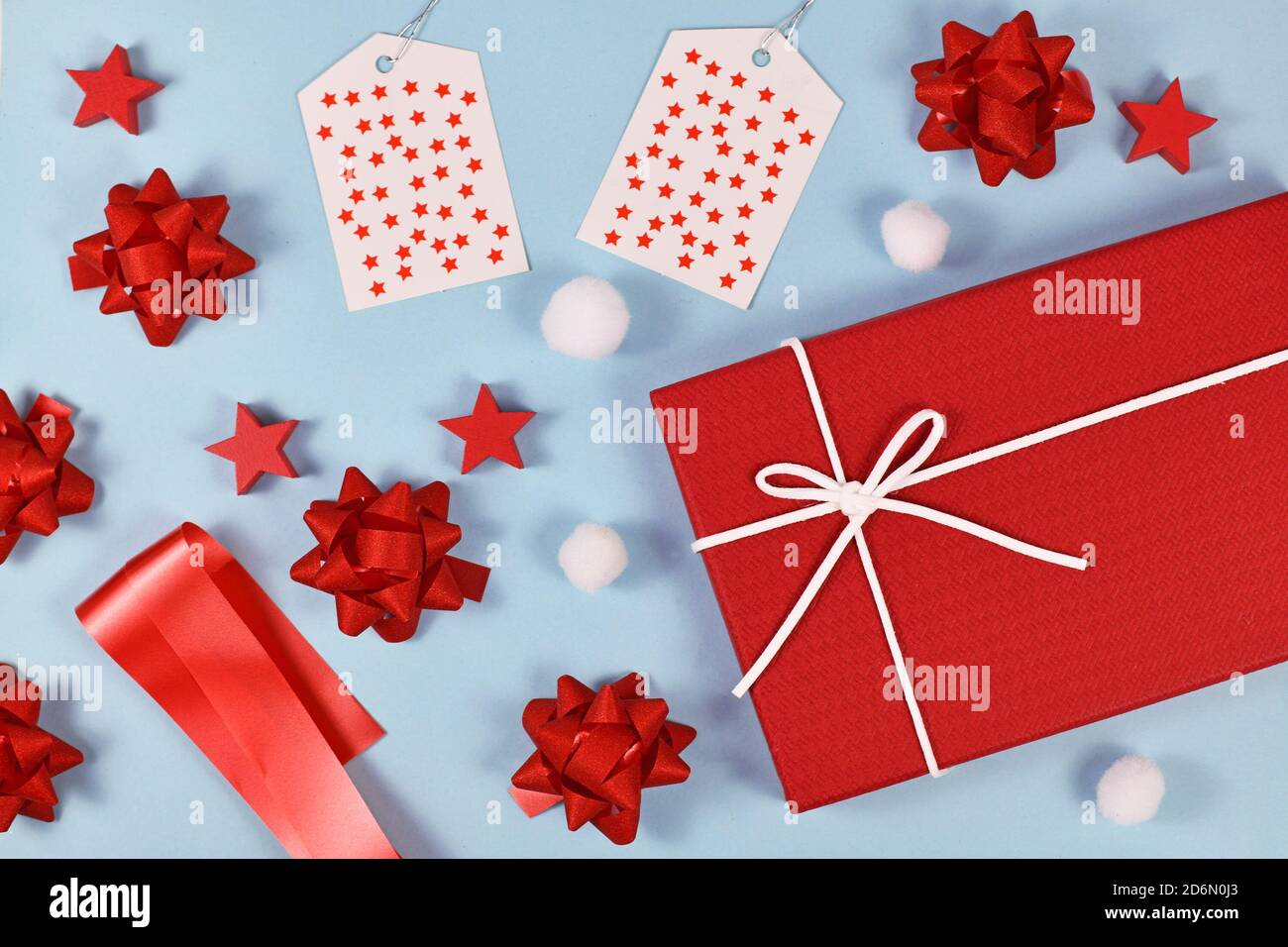 Cadeau de Noël concept d'emballage avec boîte cadeau rouge, rubans, étiquettes cadeau, ornements d'arbre et boules de neige sur fond bleu clair Banque D'Images