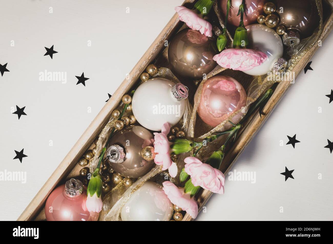 Encore vie de boules de Noël dans un plateau en bois décoré avec des boules dorées à paillettes et des œillets roses. Image matte Banque D'Images