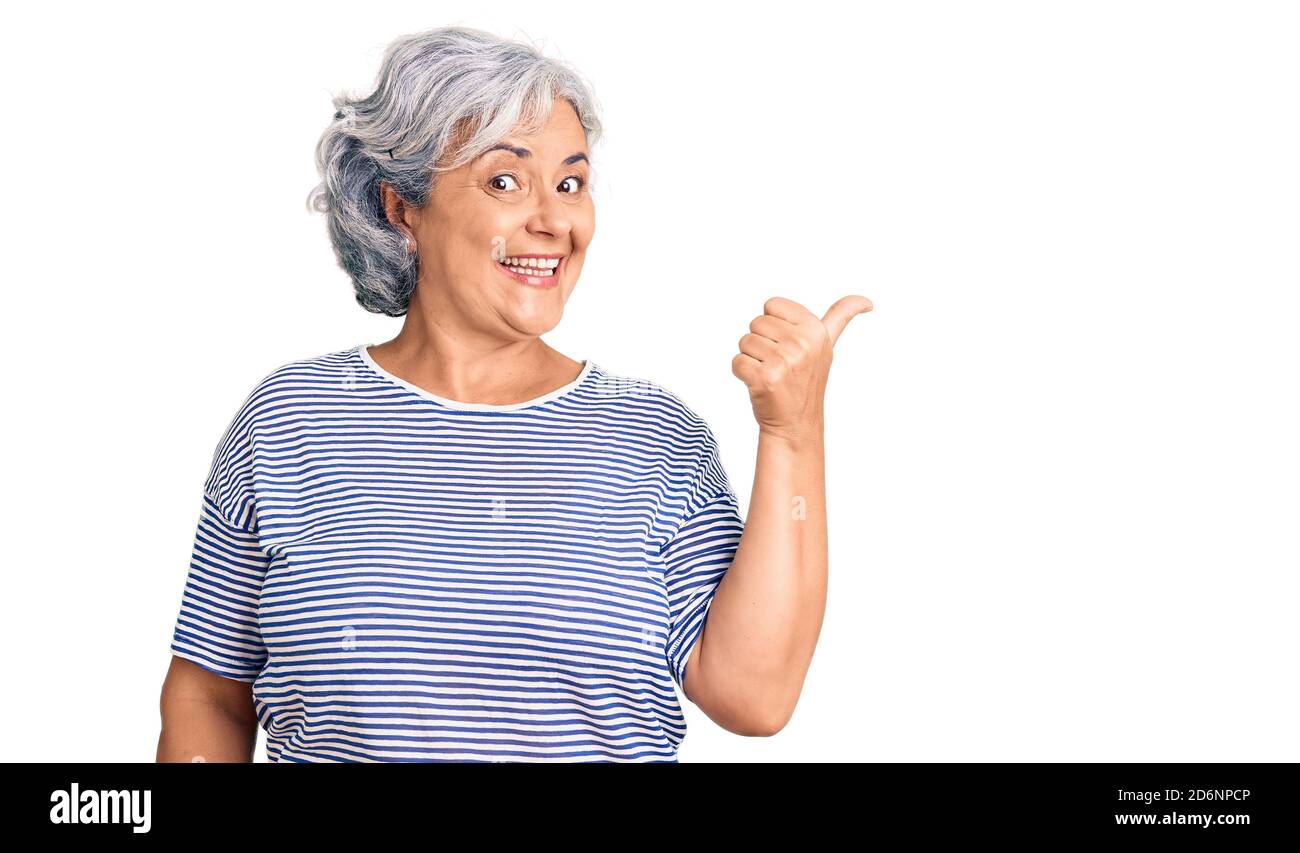 Femme âgée à cheveux gris portant des vêtements rayés décontractés souriant avec le visage heureux regardant et pointant vers le côté avec le pouce vers le haut. Banque D'Images