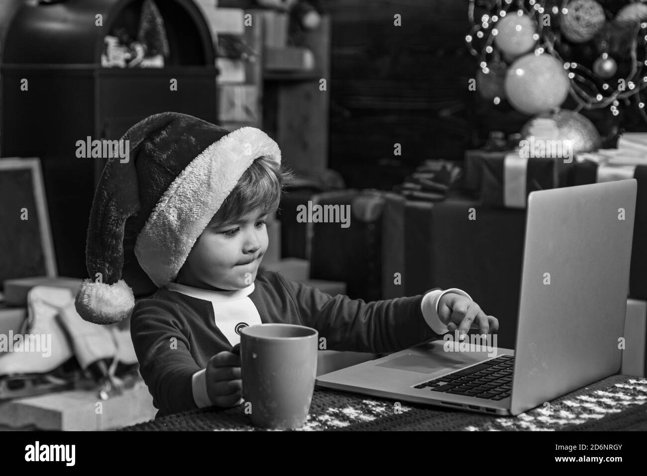 Joyeux Noël et Bonne Année. Le jeune Père Noël utilise un ordinateur portable dans son atelier. Cadeaux de Noël avec e-commerce. Banque D'Images