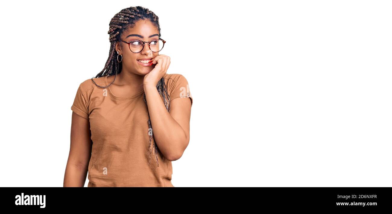 Jeune afro-américaine femme avec des tresses portant des vêtements et des lunettes décontractés ayant l'air stressé et nerveux avec les mains sur la bouche piquant des ongles Banque D'Images