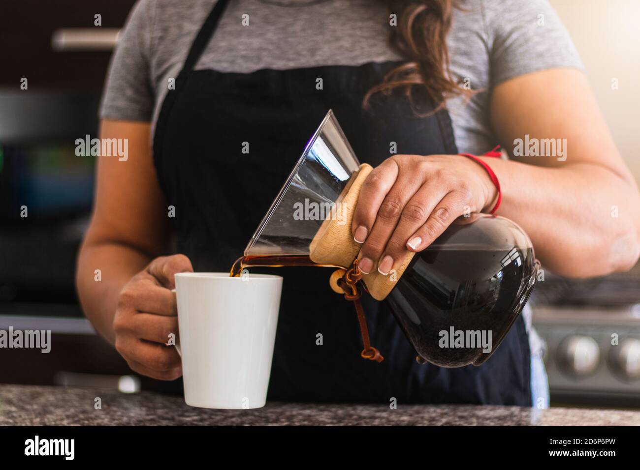 Une femme hispanique Barista verse du café dans une tasse blanche dans la cuisine familiale. Femme noire tenant verser sur la cafetière le matin Banque D'Images