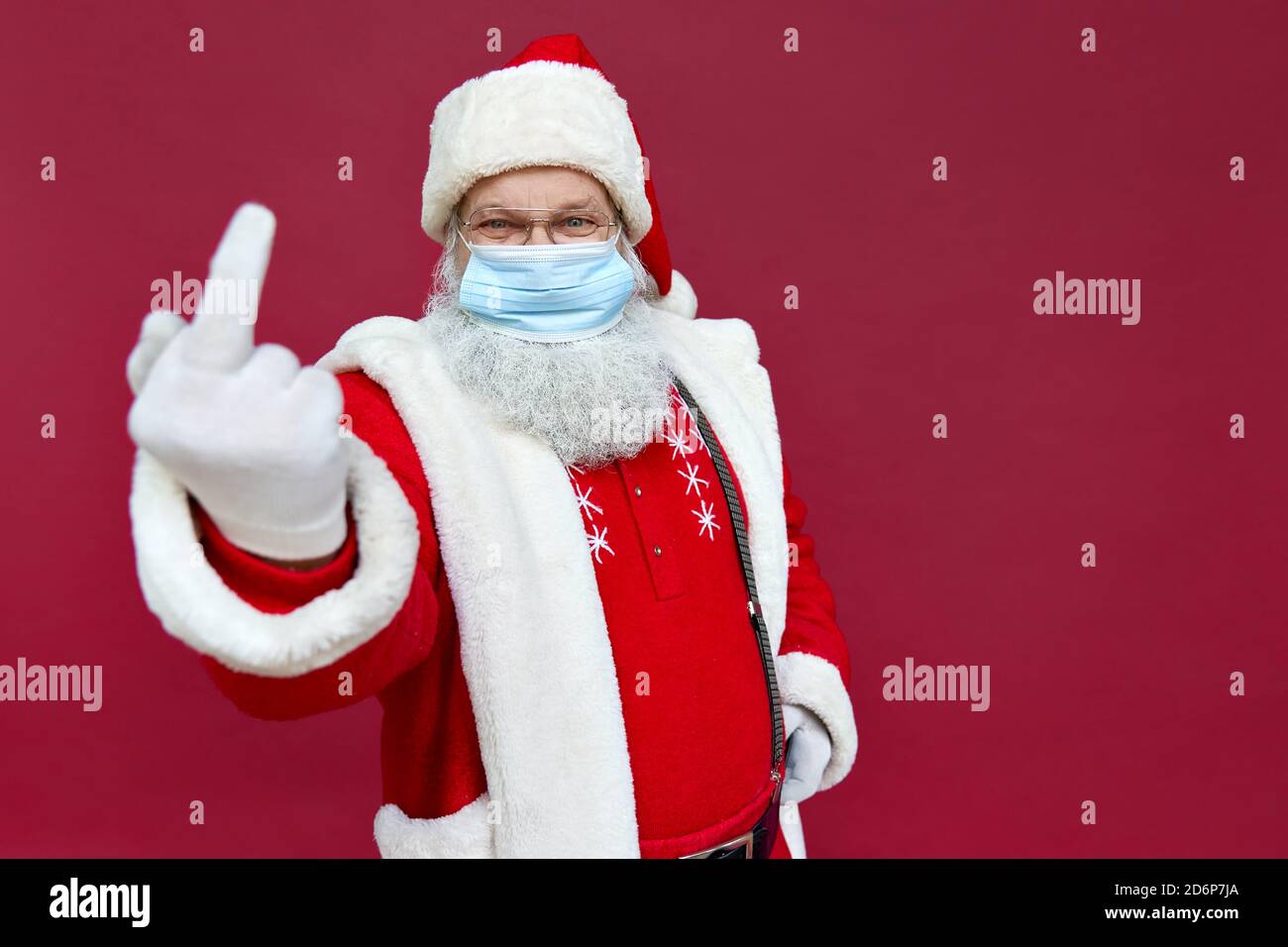 Le Père Noël porte un masque facial montrant le doigt du milieu sur fond rouge. Banque D'Images