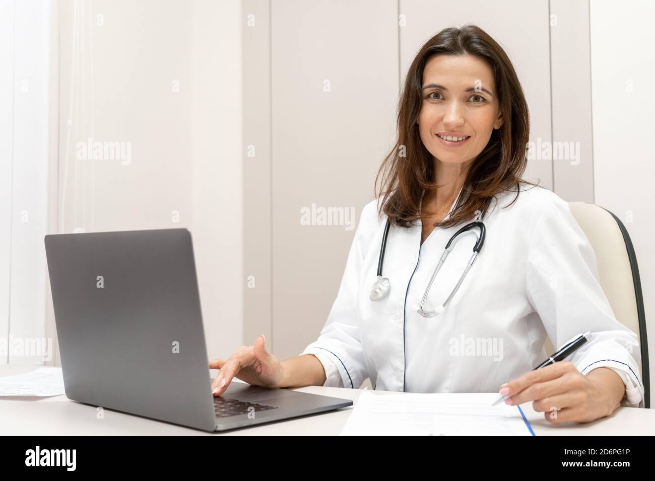 Portrait d'une femme médecin assise sur le bureau et souriant à l'appareil photo. Banque D'Images