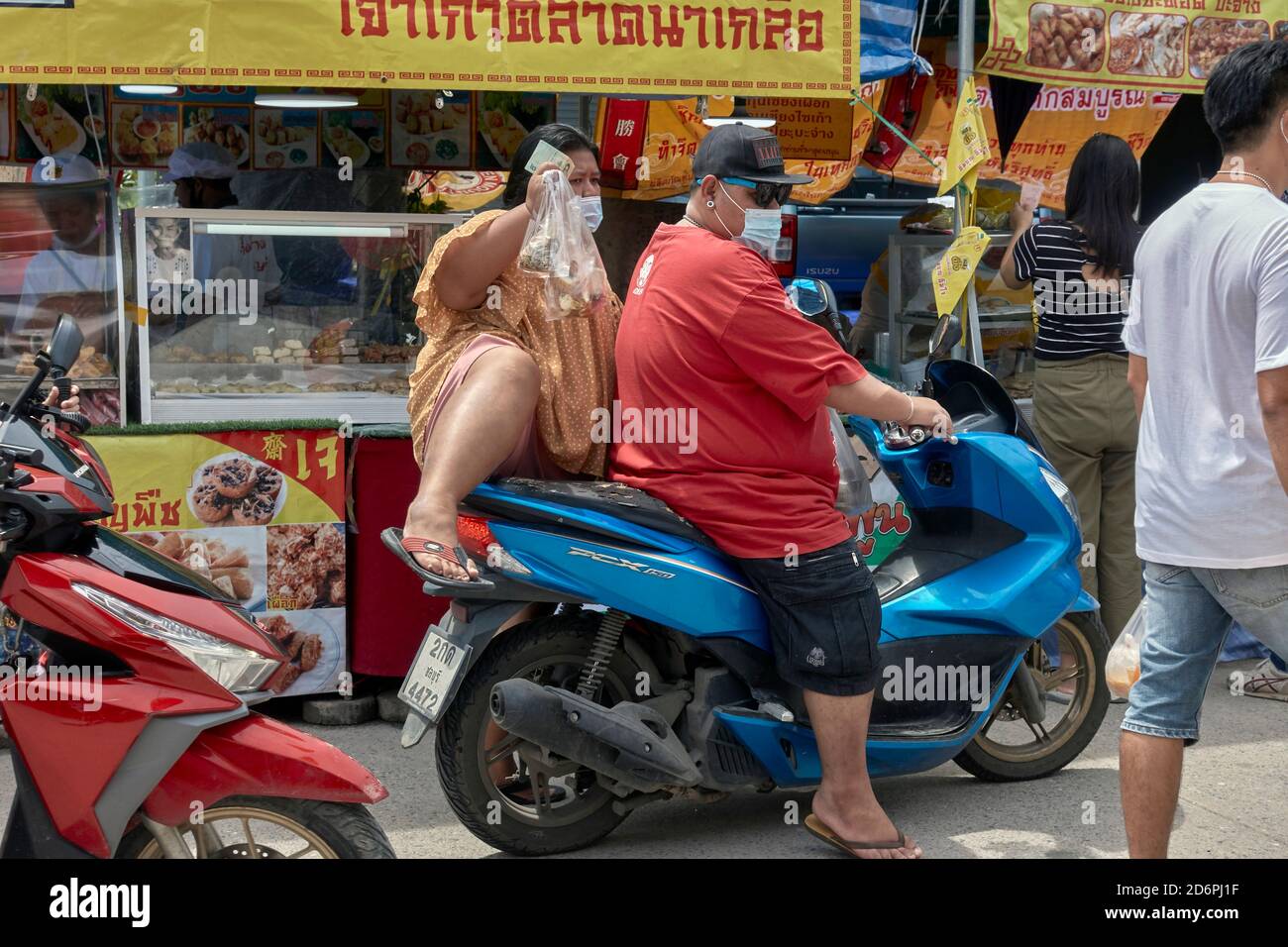 Un couple obèse faisant une moto sur un marché alimentaire de rue ayant collecté de la nourriture dans une cabine. Thaïlande Banque D'Images