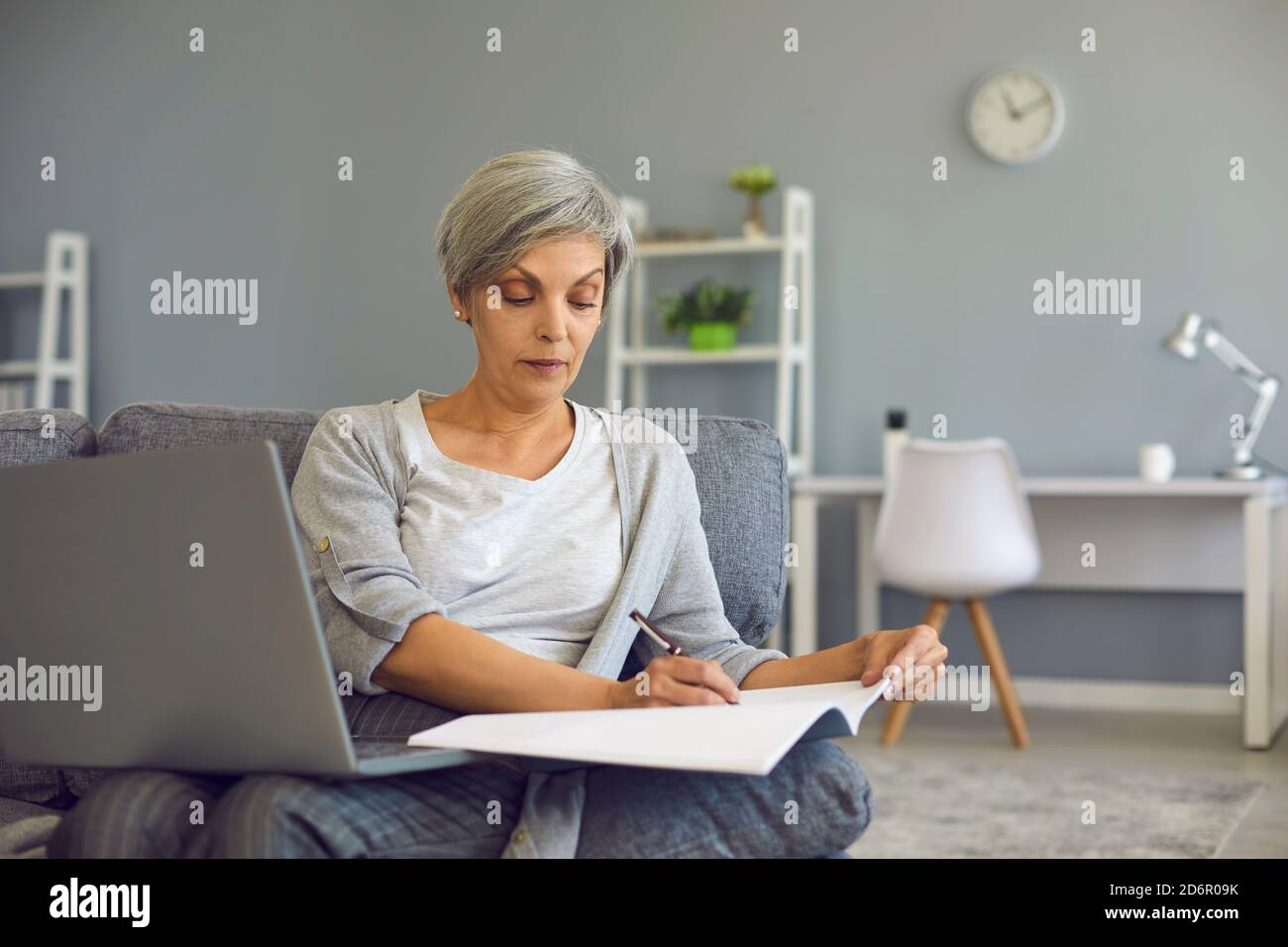 Femme senior prenant des notes pendant la leçon en ligne sur ordinateur portable à accueil Banque D'Images