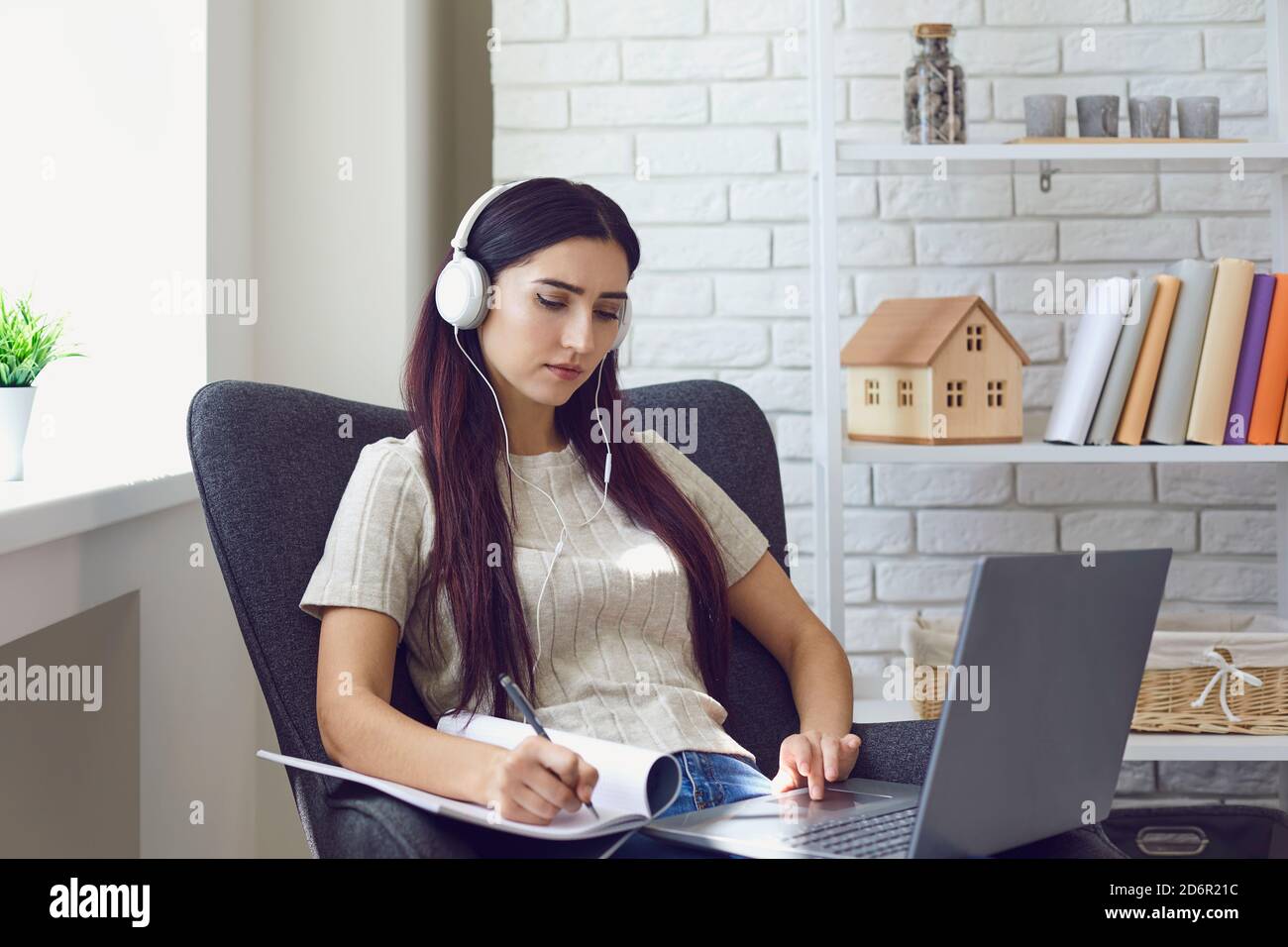 Femme dans le casque et de prendre des notes pendant la leçon en ligne à la maison sur un ordinateur portable Banque D'Images