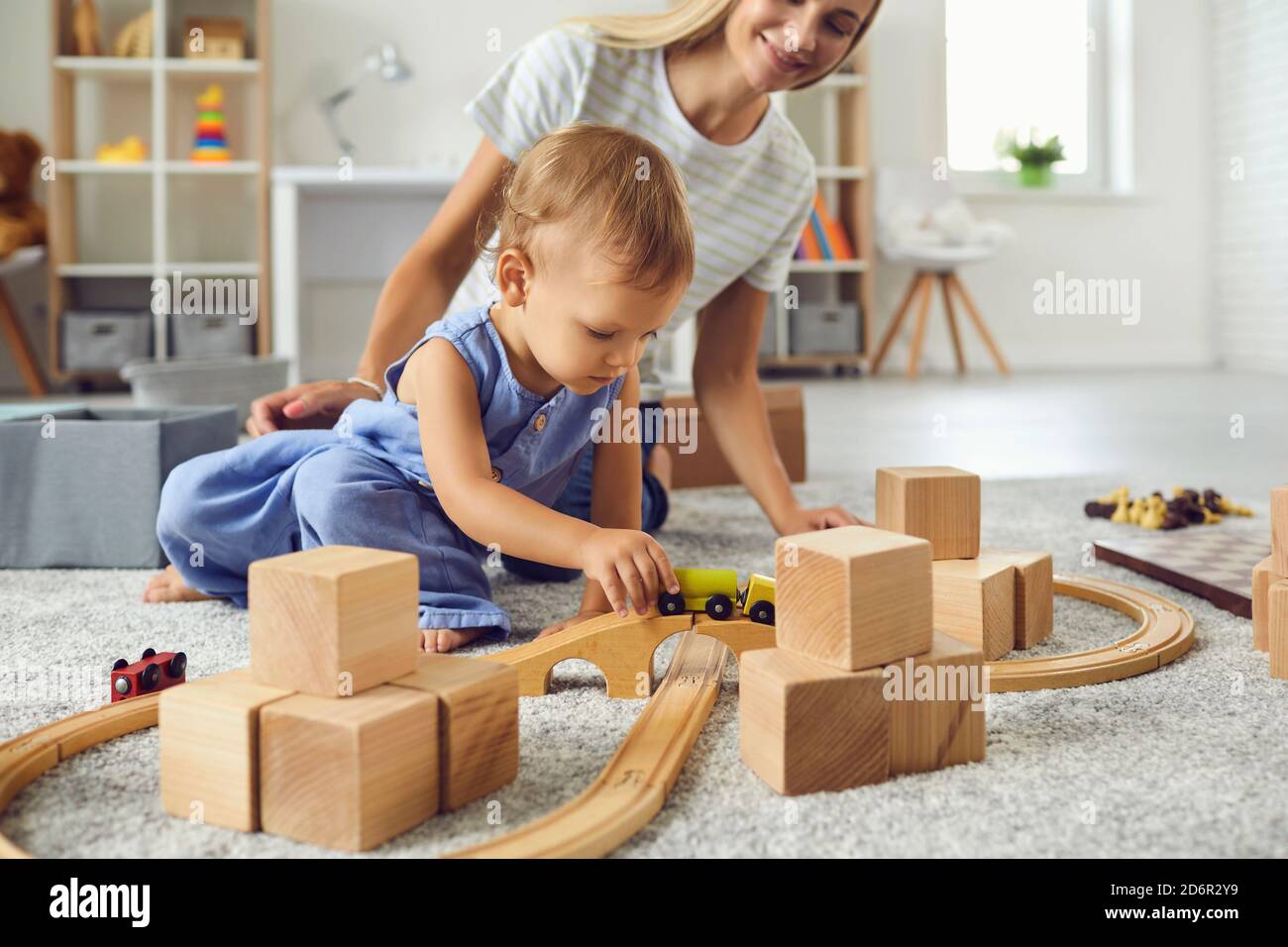Jeune nounou et petit garçon jouant avec des blocs de bois dedans chambre moderne et confortable pour bébé Banque D'Images