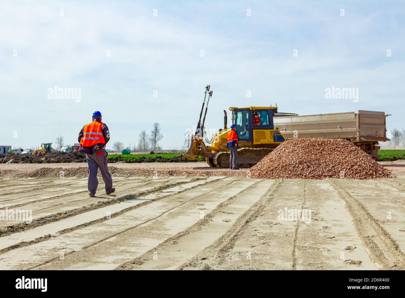 La vue sur le travailleur de la construction, le superviseur, avec gilet de sécurité et casque donne des instructions aux travailleurs du bulldozer et du conducteur de camion après le déchargement de la fract Banque D'Images