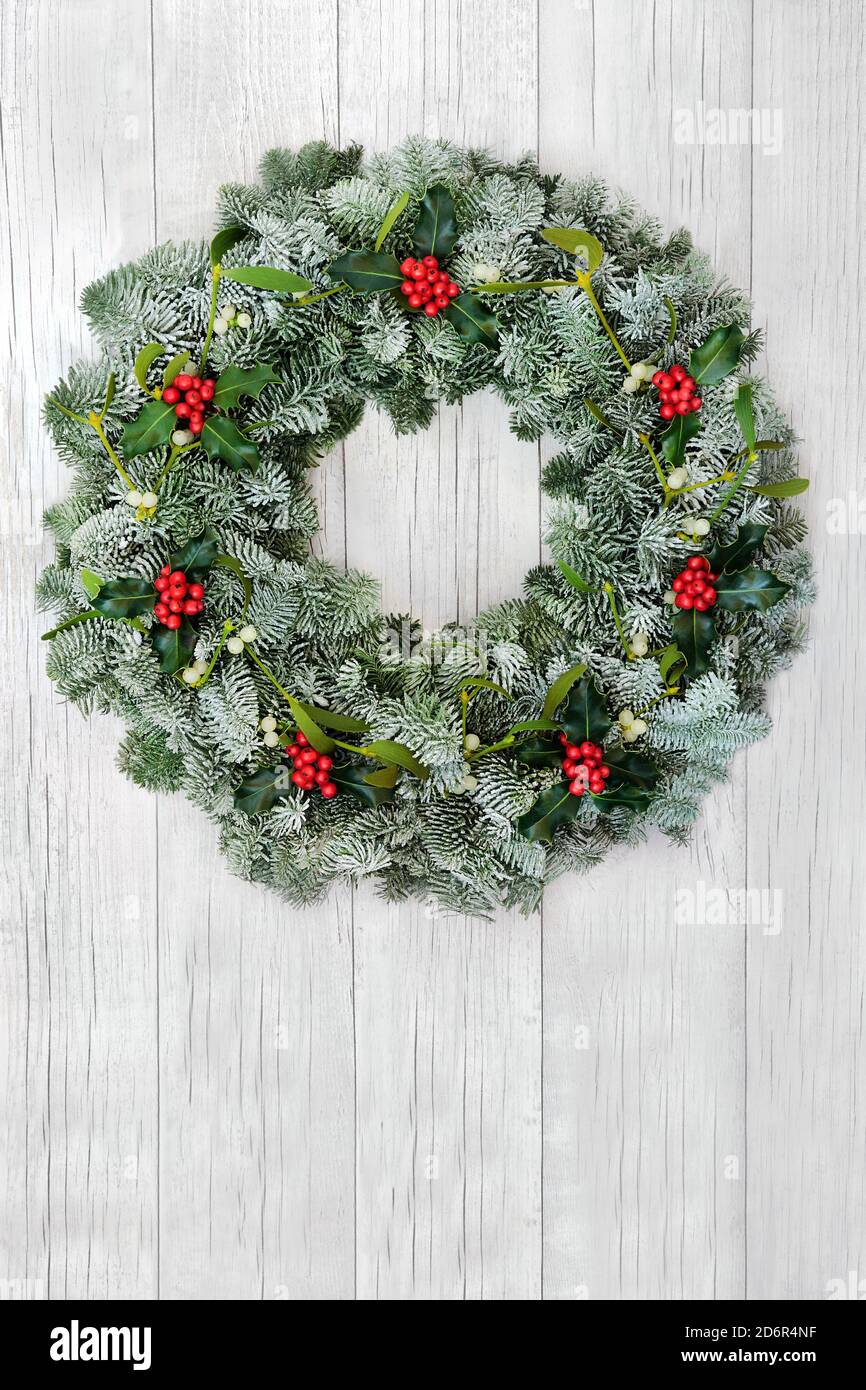 Couronne de verdure naturelle pour Noël avec sapin d'épicéa recouvert de neige, houx et GUI sur fond de bois blanc rustique. Composition traditionnelle Banque D'Images Couronne de verdure naturelle pour Noël avec sapin d'épicéa recouvert de neige, houx et GUI sur fond de bois blanc rustique. Composition traditionnelle Banque D'Images