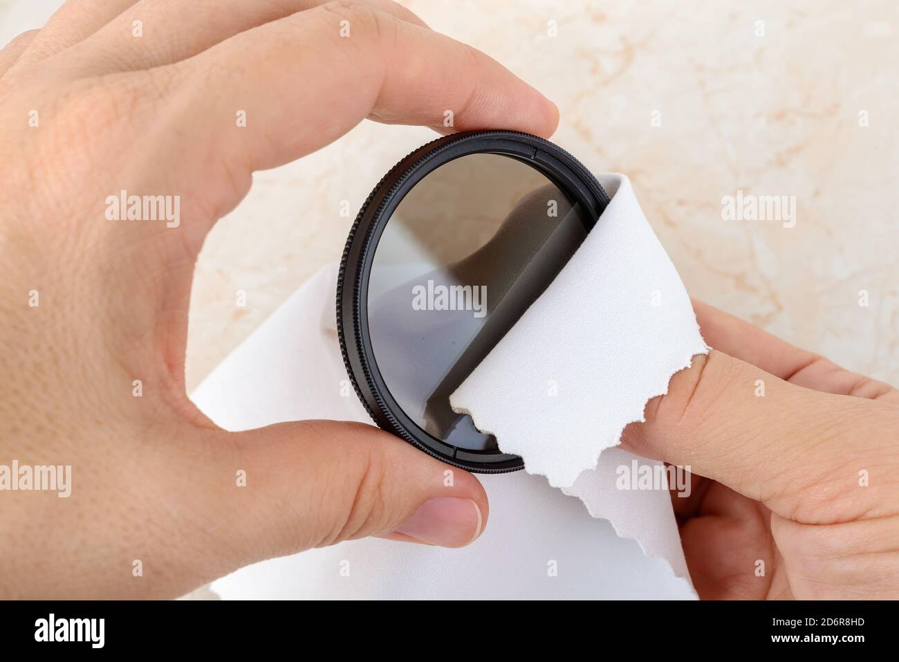 Mains essuyant un filtre polarisant de caméra avec un chiffon en microfibre blanc. Élimination de la poussière et des empreintes digitales des équipements photographiques. Entretien. Banque D'Images