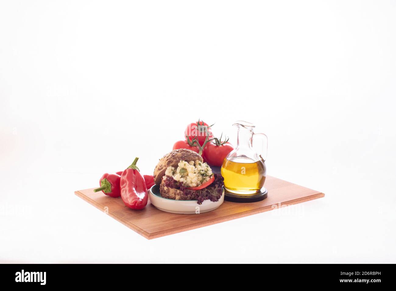 Sandwich au fromage blanc et au tomatoe avec une bouteille d'huile d'olive, du poivre de capia rouge et un bouquet de tomates servi sur une assiette en bois Banque D'Images