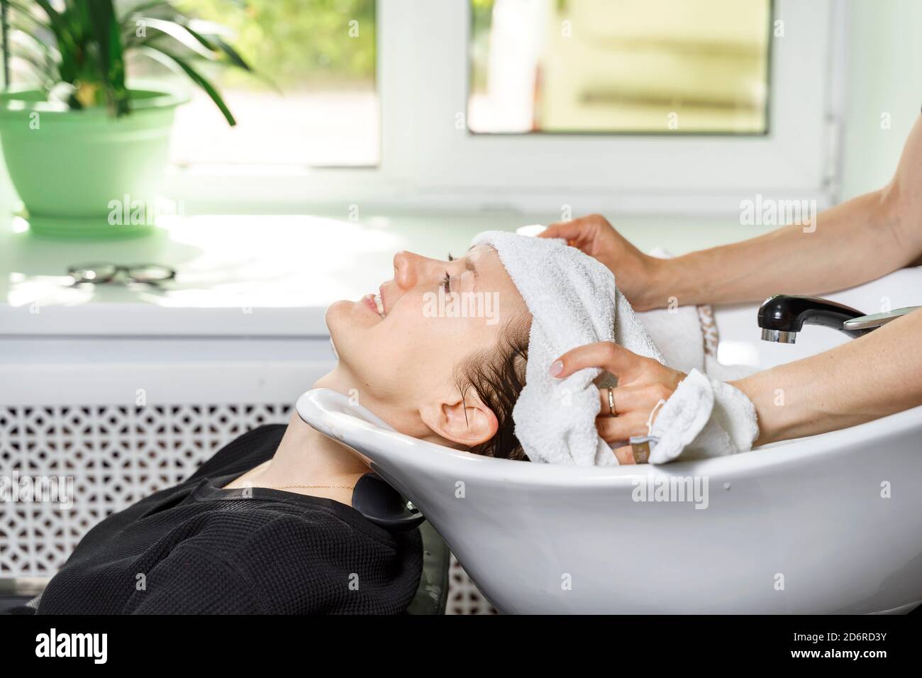coiffeur couvre les cheveux du client avec une serviette. la jeune femme se lave les cheveux dans un salon de beauté Banque D'Images