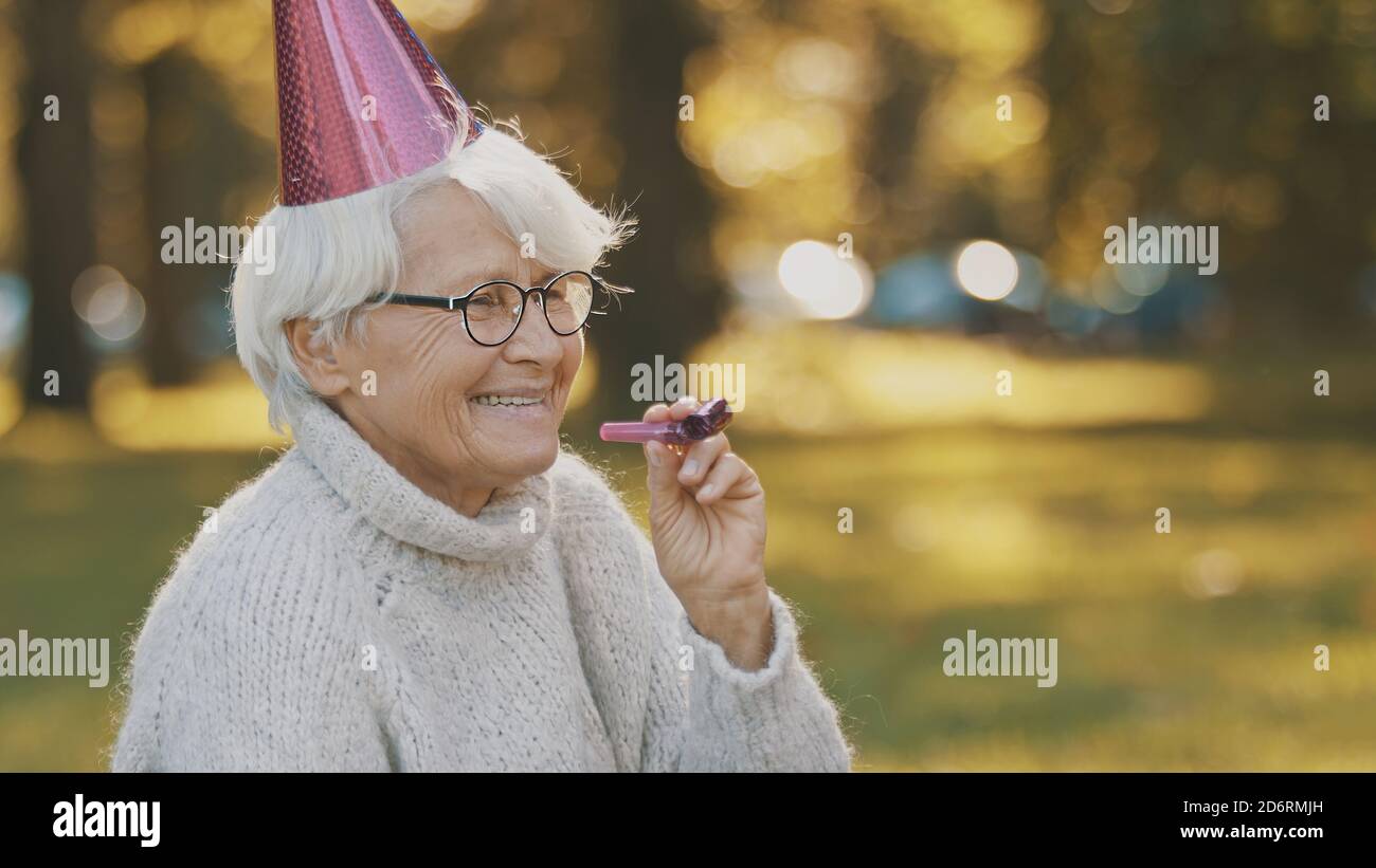 Femme âgée avec chapeau de fête et sifflet enjouant la célébration d'automne dans le parc. Photo de haute qualité Banque D'Images