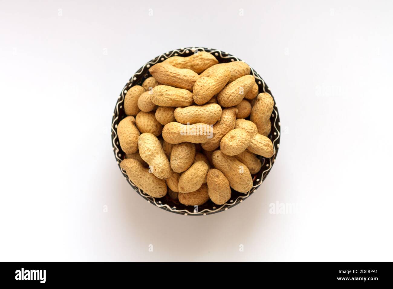 Arachides crues dans la coquille sur la coupe d'argile sur fond blanc. Vue de dessus Banque D'Images