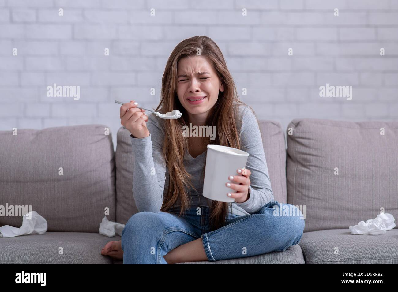 Une alimentation émotionnelle. Femme stressée pleurant sur le canapé avec un seau de glace, regardant un film triste et se sentant déprimé Banque D'Images