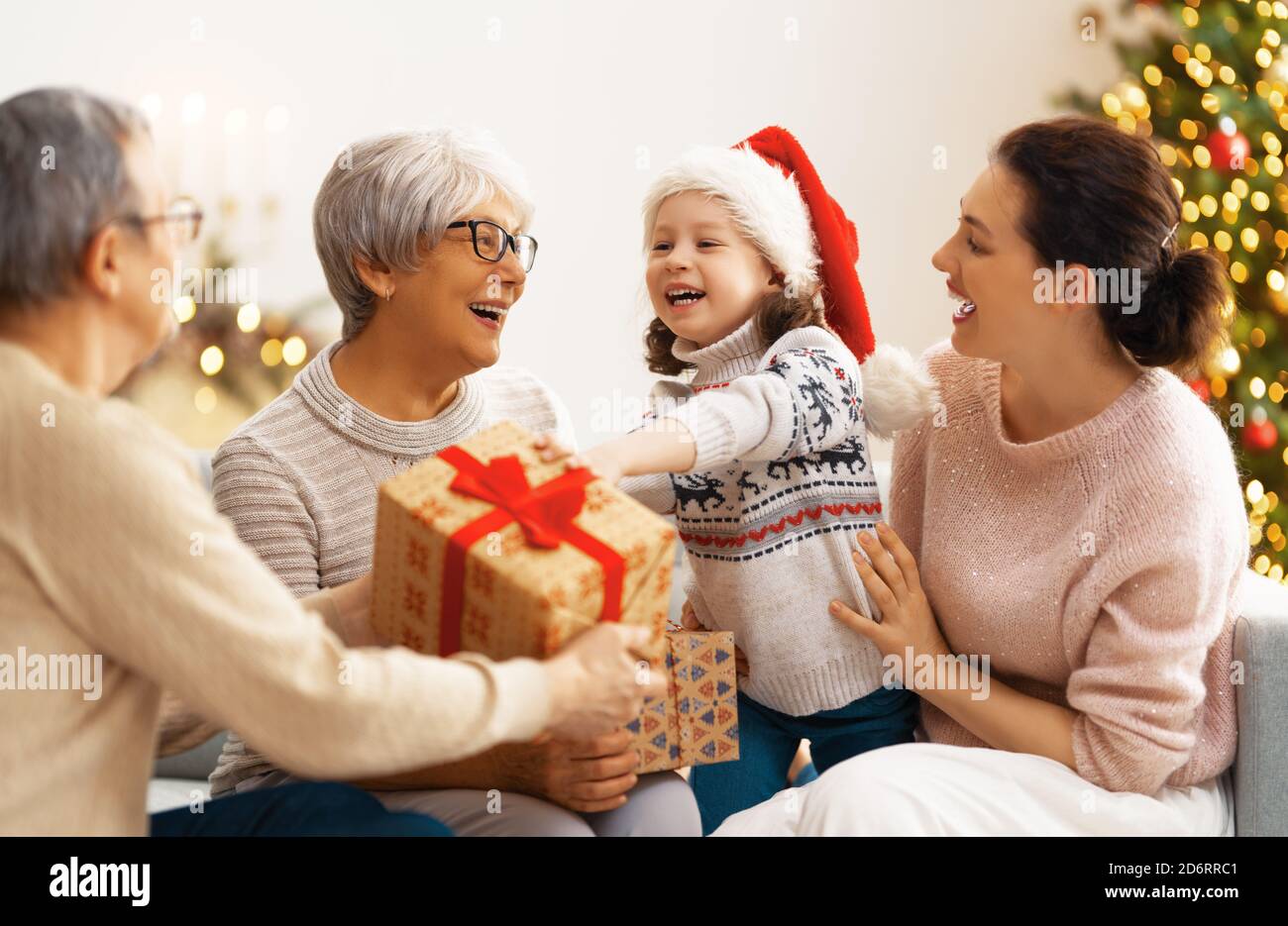 Joyeux Noël et joyeuses fêtes ! Grand-mère, grand-père, mère et enfant échangeant des cadeaux. Parents et filles s'amuser près de l'arbre à l'intérieur. Affectueux famil Banque D'Images
