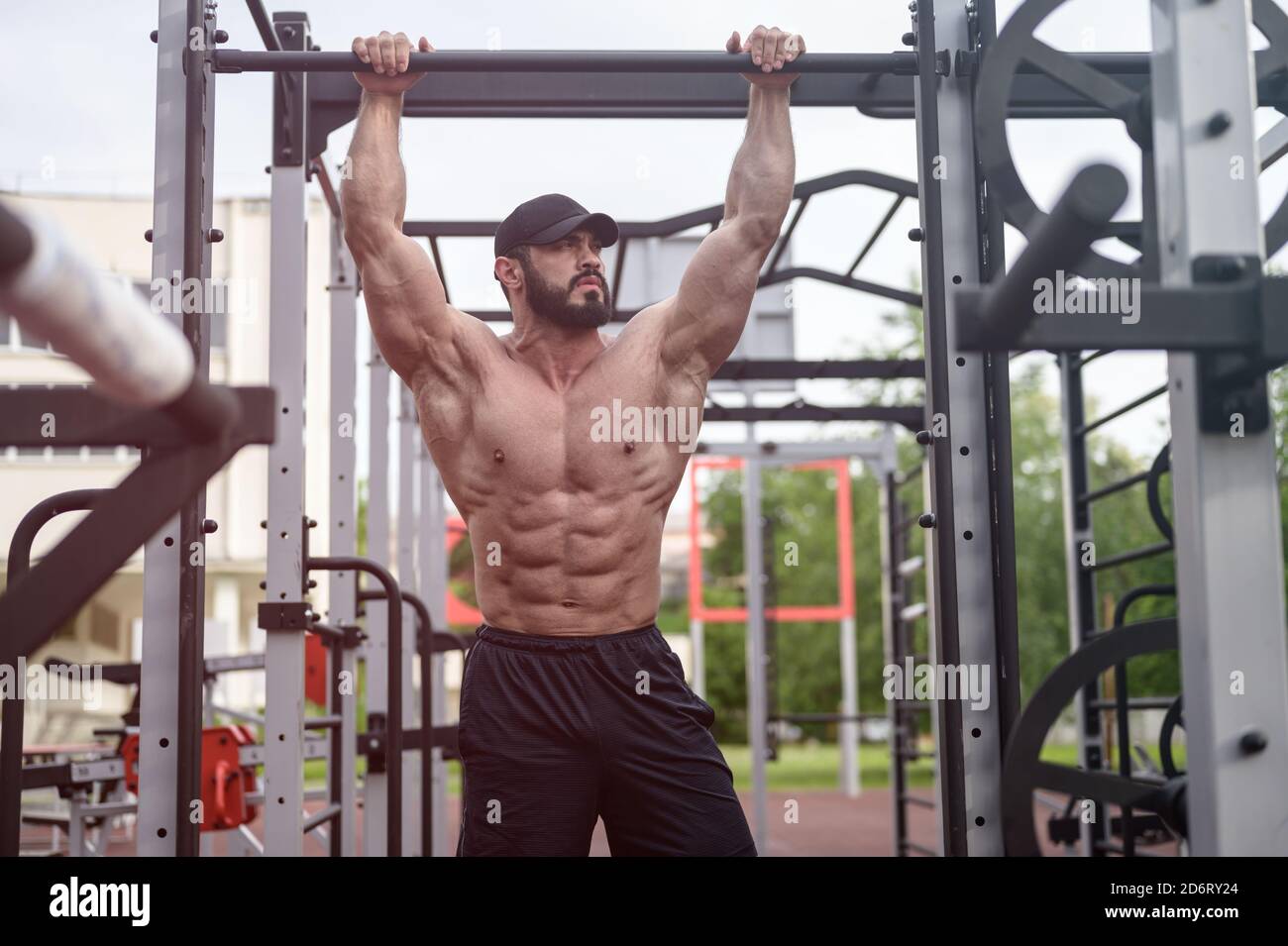 active jeune homme barbu fort tenant la barre transversale pendant l'entraînement de rue équipements de sport de fitness pendant les activités de loisirs Banque D'Images