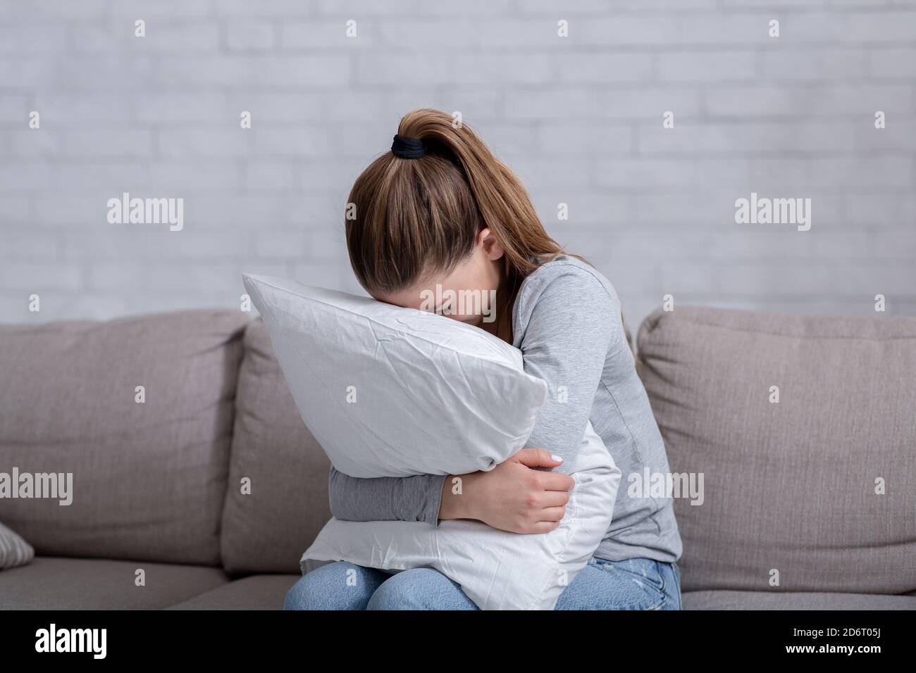 Jeune femme avec dépression embrassant l'oreiller et pleurant sur le canapé à la maison Banque D'Images