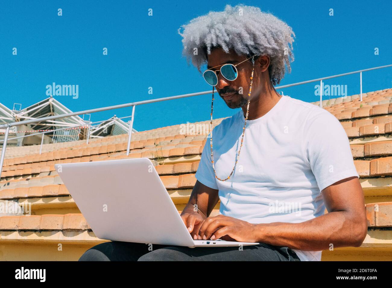 Afro et homme noir avec des lunettes de soleil travaillant avec son ordinateur portable dans la rue. Travailler avec l'ordinateur portable à l'extérieur. Homme noir travaillant sur l'ordinateur. Banque D'Images