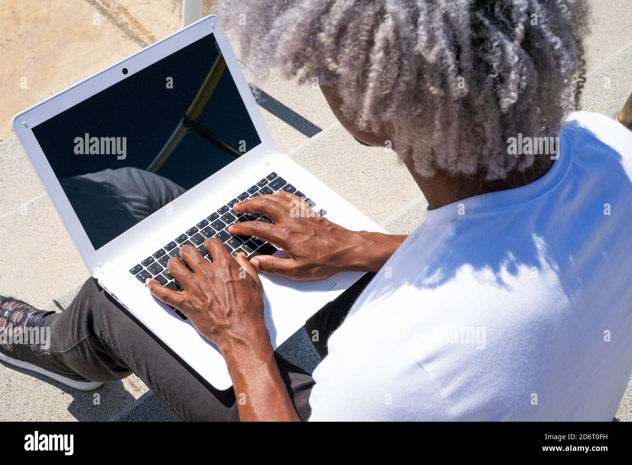Vue de dessus d'un homme noir travaillant sur un ordinateur portable blanc. Concept de recherche de travail et de travail à l'extérieur. Banque D'Images