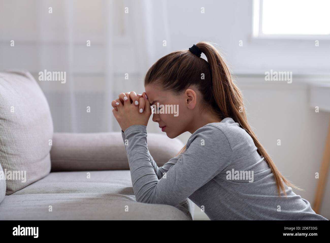 Vue latérale de la jeune femme désespérante priant à Dieu pour l'aide ou la consolation sur le canapé à la maison, l'espace de copie Banque D'Images