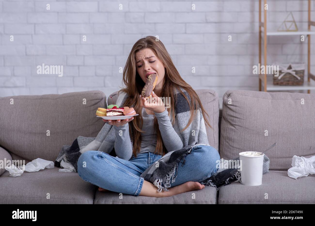 Concept de nourritures de confort et de manger de stress. Une jeune femme frustrée dévore une pâtisserie sur un canapé à la maison Banque D'Images