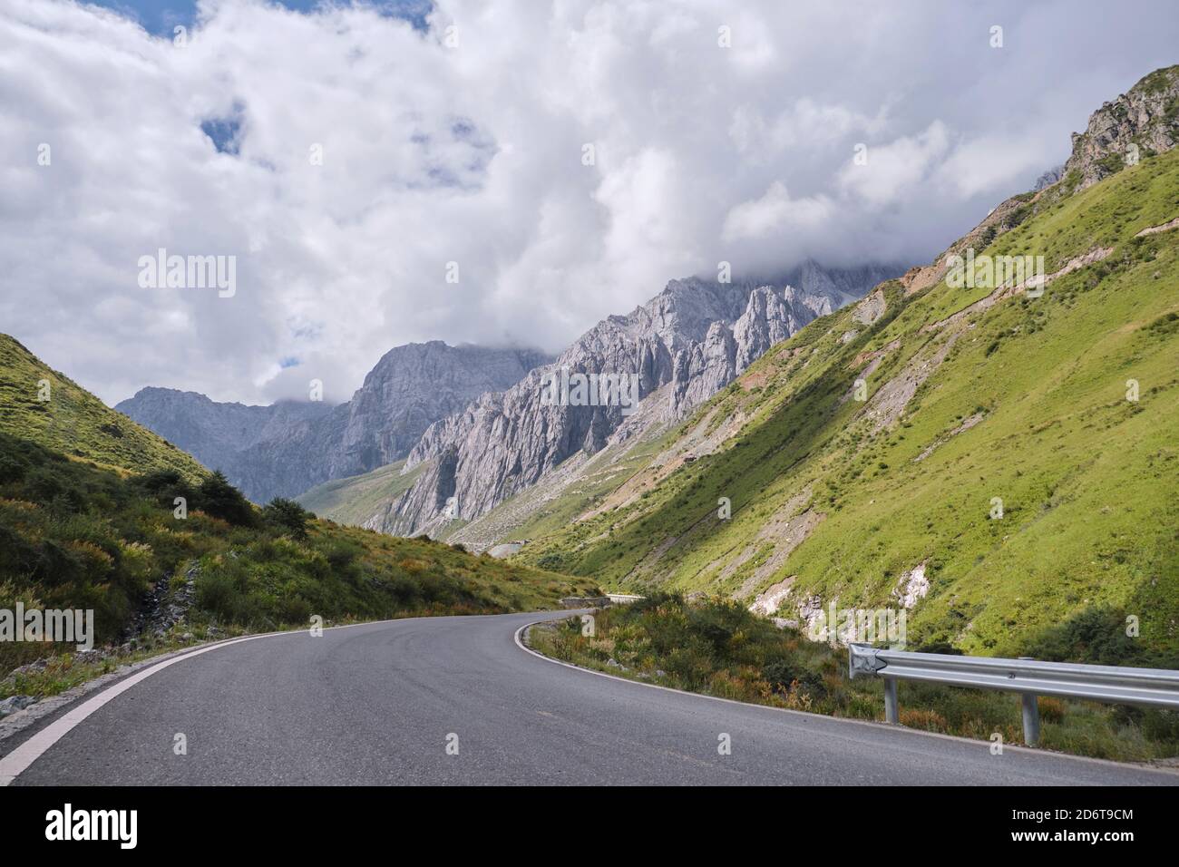 Chemin d'asphalte sinueux menant à travers des collines herbeuses recouvertes de mousse près des pics calmes disparaissent à distance Banque D'Images