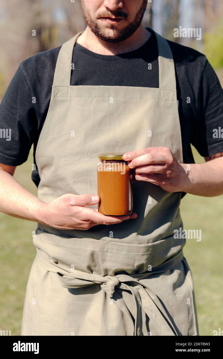 Cultivateur mâle méconnaissable debout dans un village avec un pot en verre de miel savoureux Banque D'Images